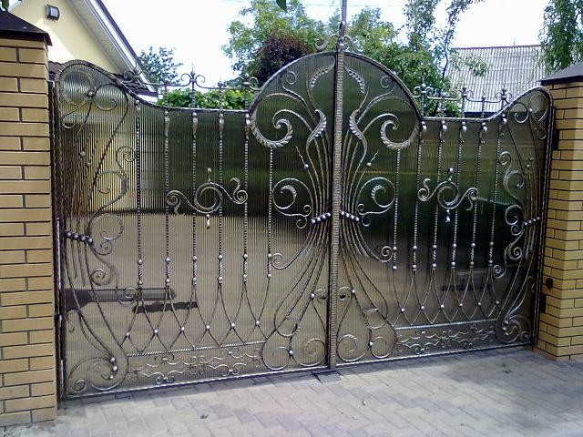 Кованый узор на воротах удачно комбинируется с мелкой сеткой и дает стильный эффект паутины
